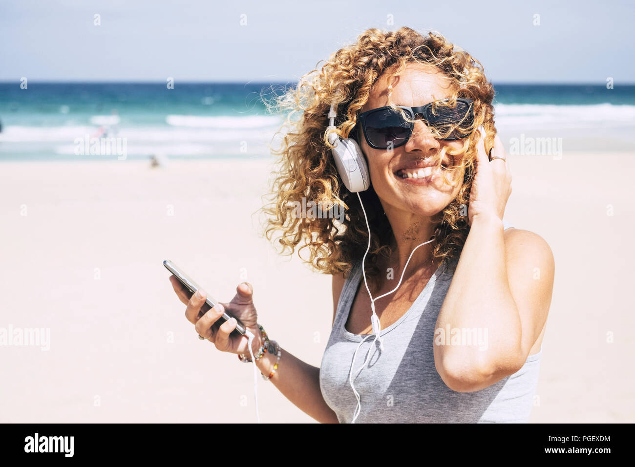 Allegro attraente bella caucasian medioevo donna sorridente in spiaggia in luogo tropicale mentre si ascolta la musica con gli smart phone. persone enjoyi Foto Stock