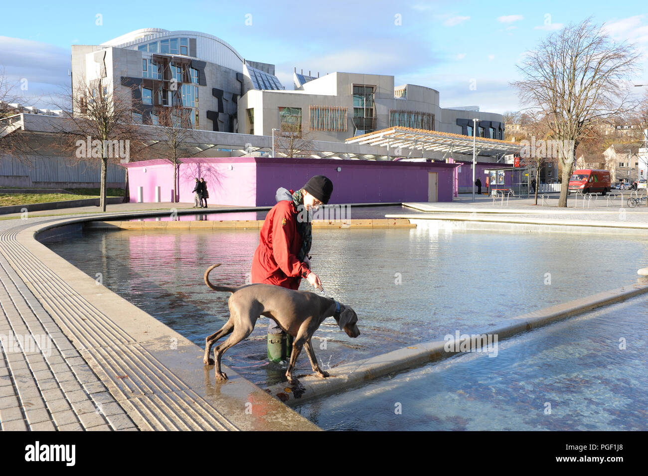 Una donna in wellie boots prende il suo cane per una racchetta nello stagno di fronte all'edificio del parlamento scozzese di Edimburgo, Scozia Foto Stock