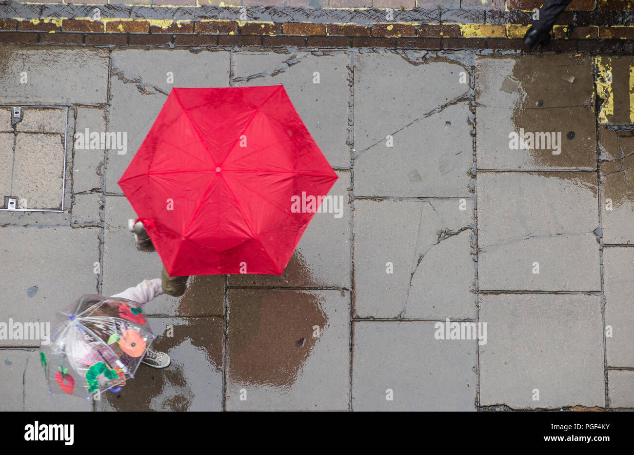 Piove e ombrelloni sono sollevate per tenere a secco su una strada di Londra - una madre e un bambino per mano con un bambini ombrello Foto Stock