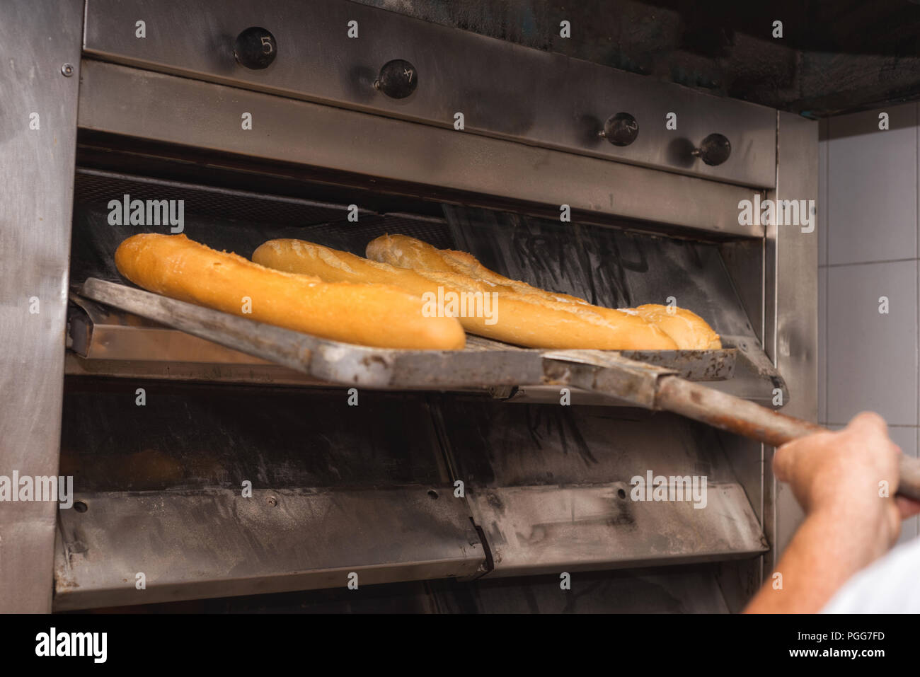 Baker tenendo fuori pane fresco dal forno industriale Foto Stock