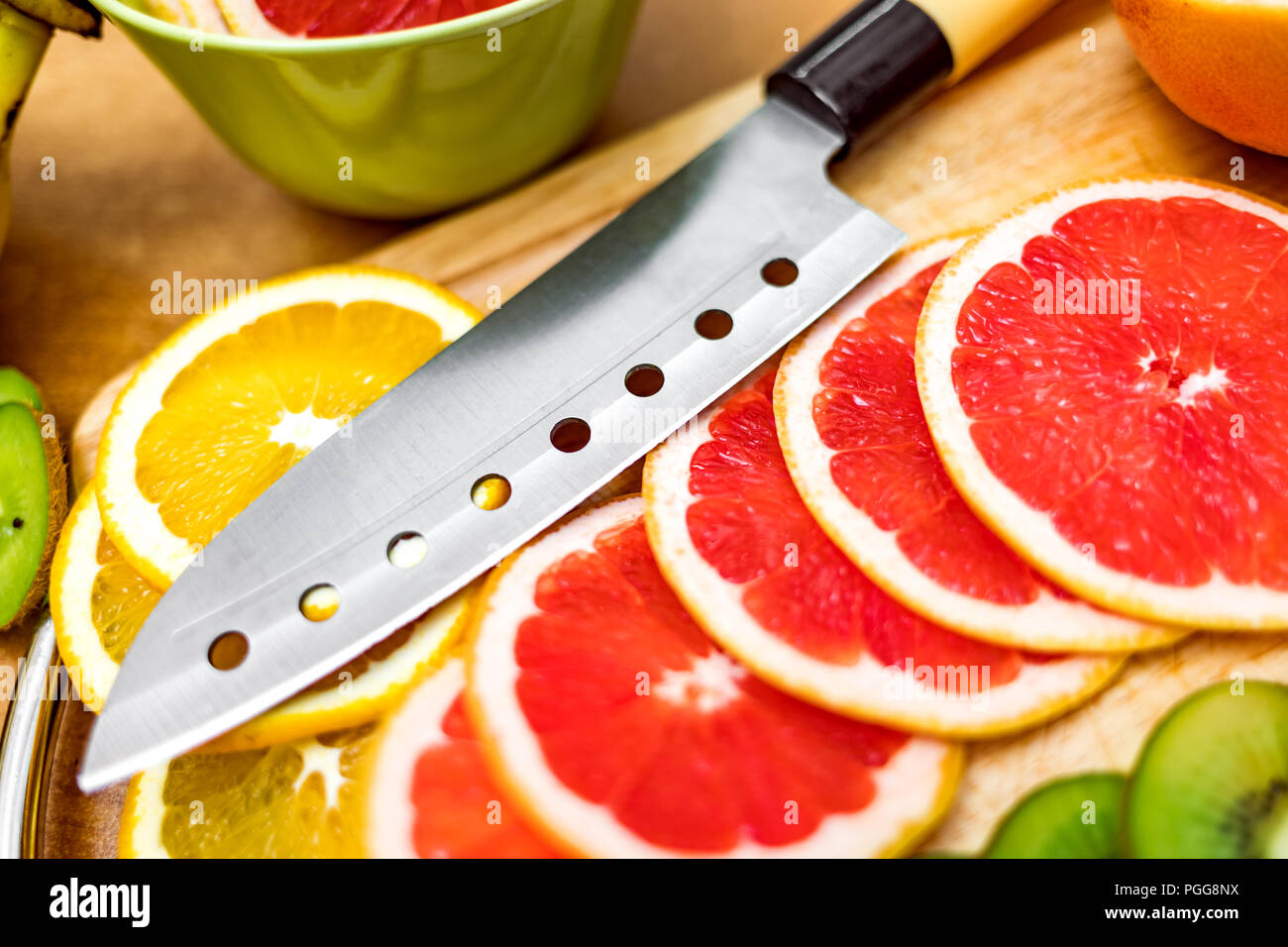 Coltello da cucina affilato sul tagliere accanto a fette di pompelmo e altri frutti Foto Stock