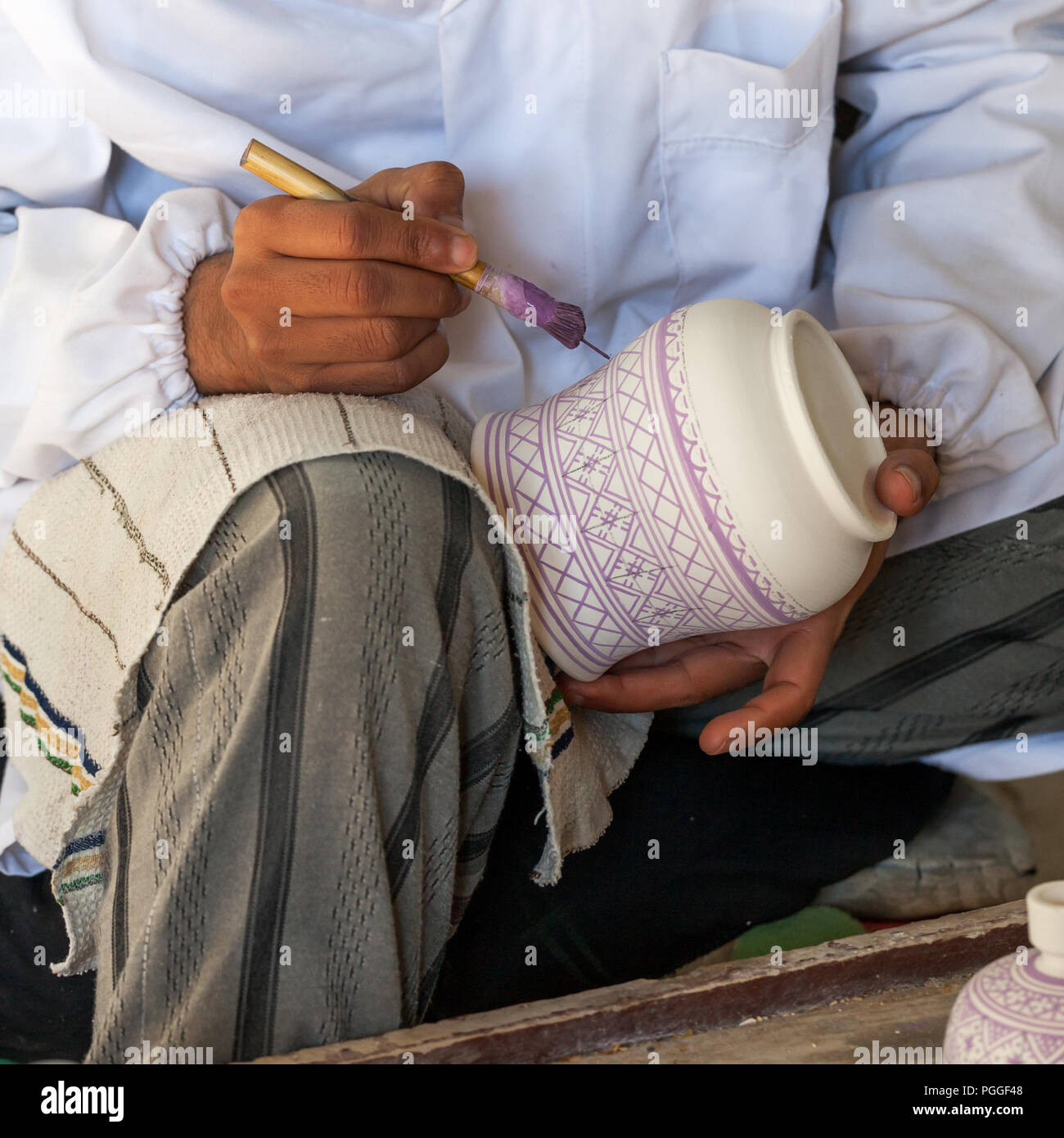 Artista marocchino dipinge disegni su un vaso di ceramica. Vista ravvicinata dell'applicazione manuale della vernice sul vaso non cotto. Foto Stock