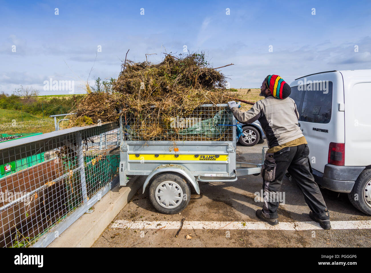 Rastafarian lo scarico di rifiuti del giardino dal rimorchio in consiglio deposito di riciclaggio skip - Francia. Foto Stock