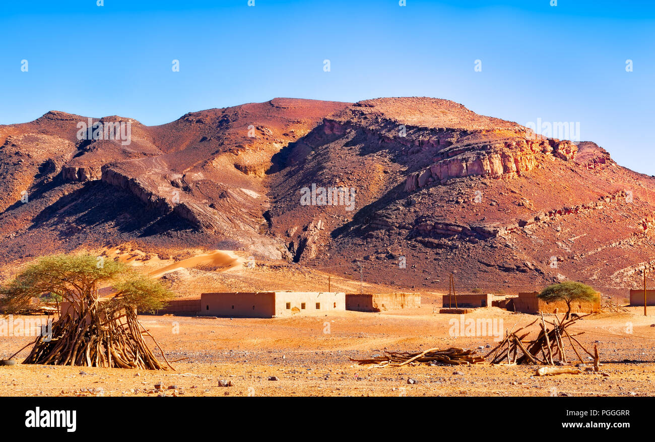 Marocchino deserto piccolo villaggio di sparse adobe bassi edifici in mattoni contro la pedemontana. Foto Stock