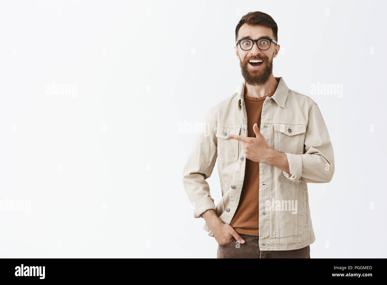 Gosh guardare come incredibile. Ritratto di impressionato entusiasta hipster ragazzo con barba lunga e breve acconciatura in nero bicchieri sorridendo ammirato rivolta verso sinistra estasiate su sfondo grigio Foto Stock