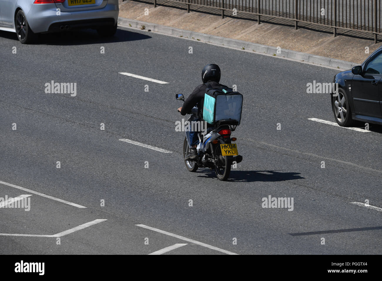 Un cavaliere deliveroo offrendo un pacchetto di cibo su un ciclomotore guidando lungo una strada a doppia carreggiata con copia spazio occupato dal di sopra. Foto Stock