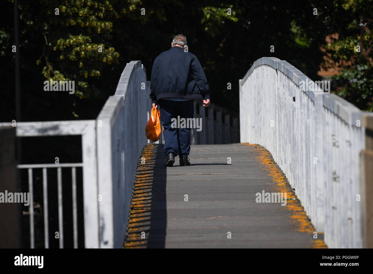 Un vecchio uomo(55-60s) cammina da sola su una passerella di distanza dalla telecamera che trasportano una plastica shopping bag. Foto Stock