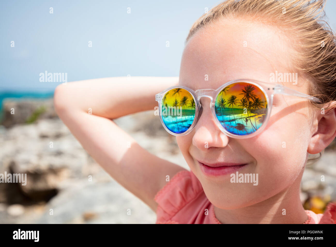 Adorabile bambina in spiaggia durante le vacanze estive indossando occhiali da sole riflettente spiaggia tropicale con palme Foto Stock