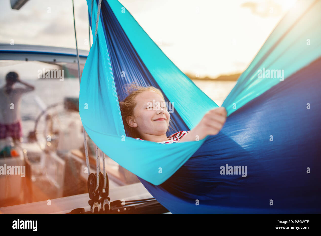 Ragazza carina godersi il tramonto rilassante nella amaca impostato sulla vela barca mentre la barca a vela in mare aperto Foto Stock