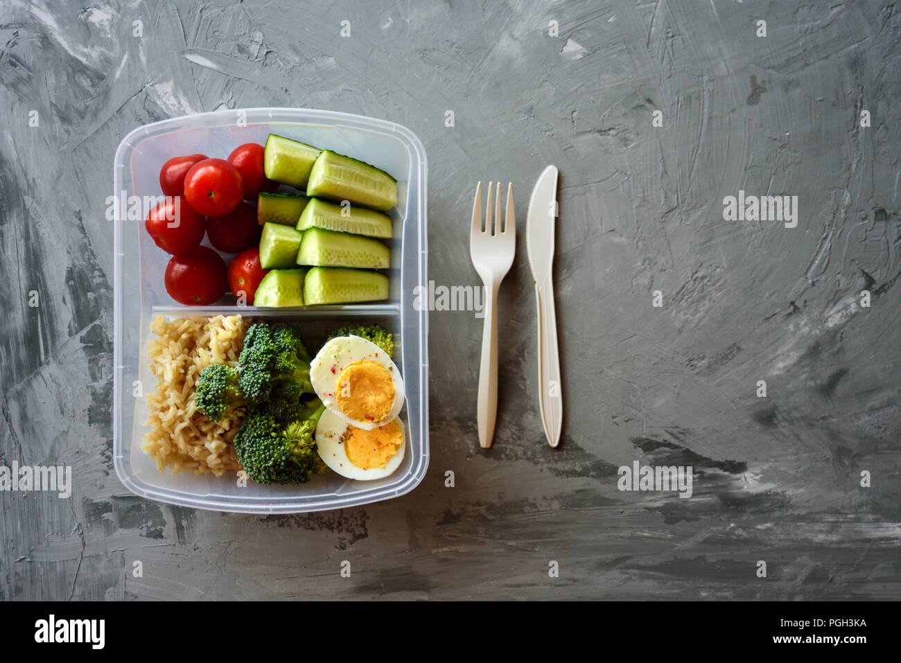 Scatola di pranzo con cibo sano. Riso, broccoli, pomodoro, cetriolo, uova, apple e acqua. Sul cemento grigio sfondo Foto Stock