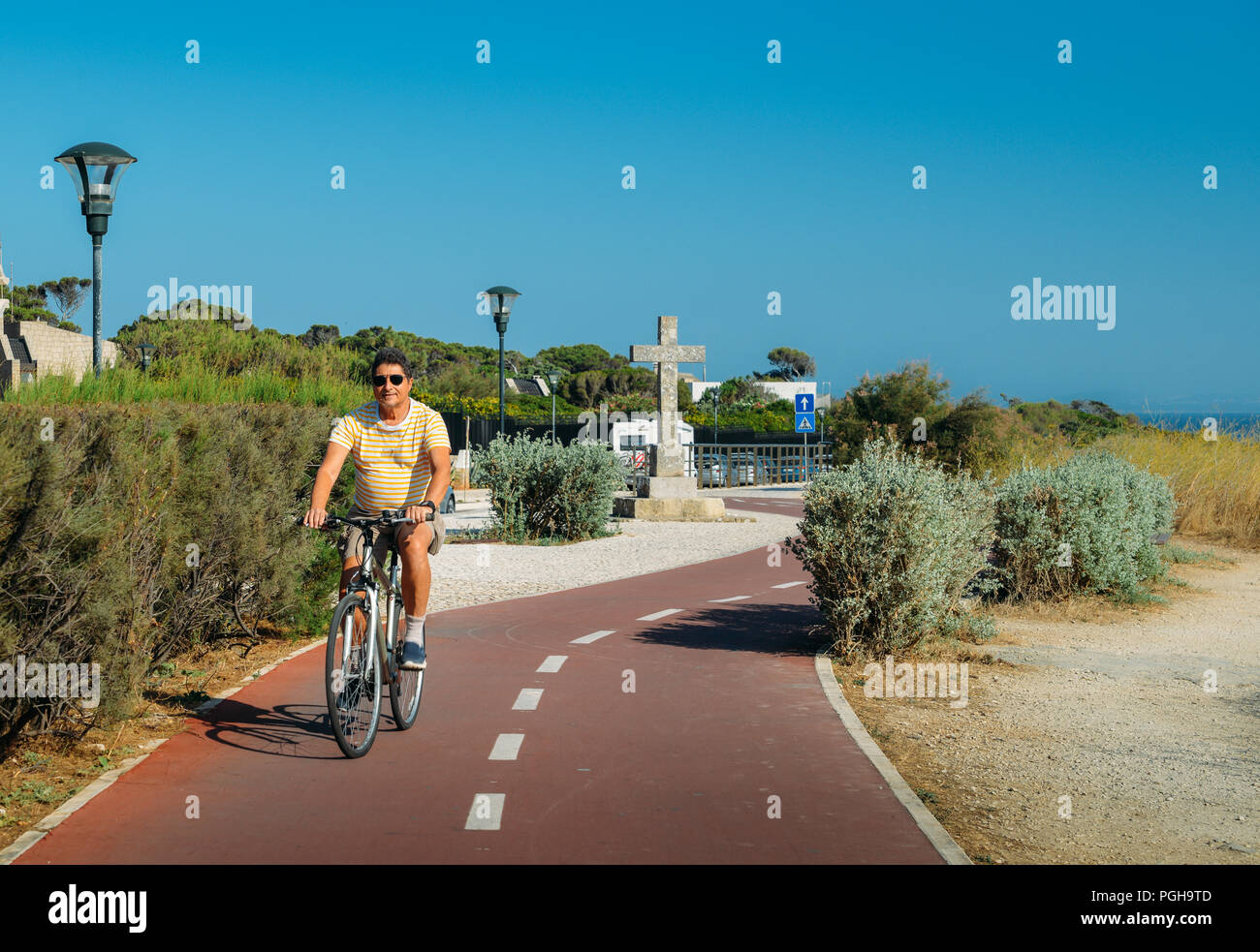 Uomo maturo (55-60) cicli lungo un percorso ciclabile vicino a Praia do Guincho e Roca do Cabo vicino a Cascais, Portogallo durante un giorno di estate Foto Stock
