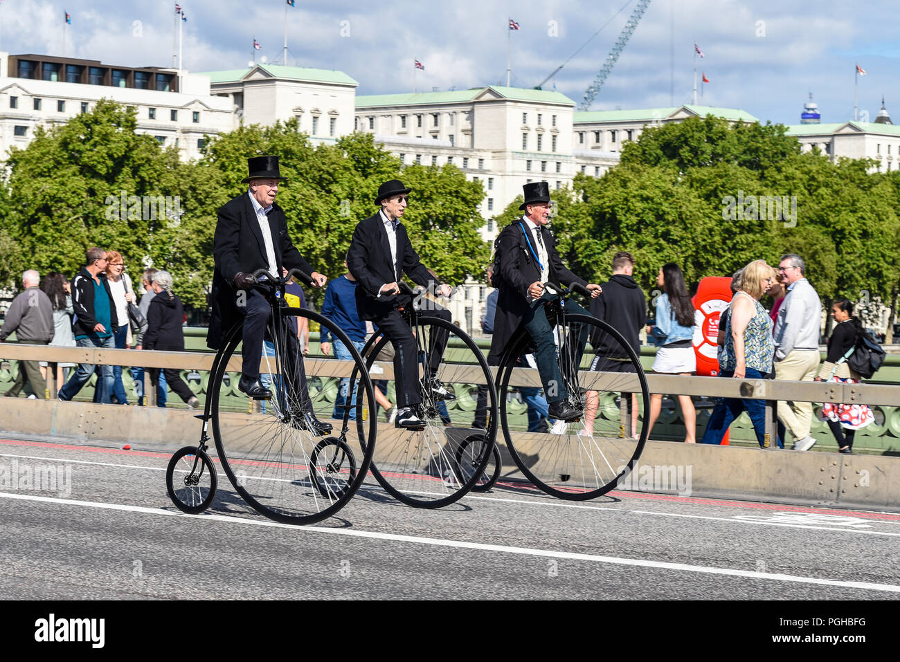 Tre Penny Farthing ciclisti giro attraverso Westminster Bridge, Londra, Regno Unito. Colleghi piloti. Penny farthings da UDC, monociclo dot com. Top cappelli Foto Stock