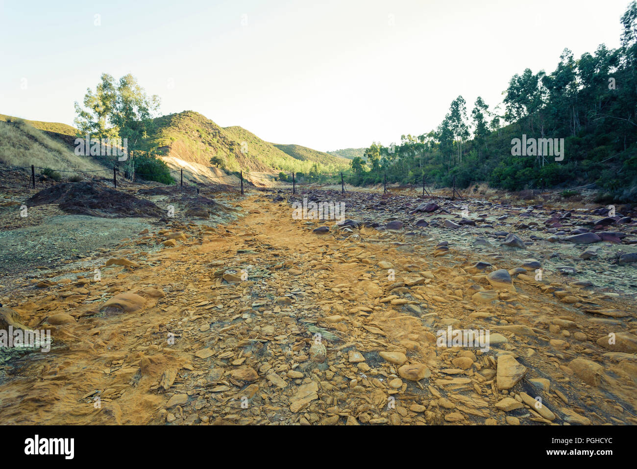 Riverbed a secco con pietre di colore arancione tra montagne di eucalipto con cielo blu sullo sfondo Foto Stock