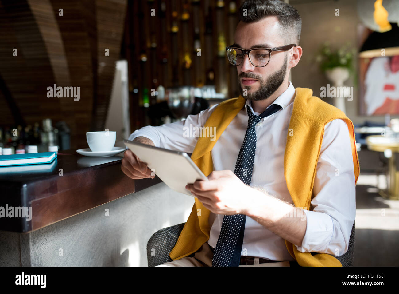 Ritratto di bello imprenditore barbuto seduto al banco bar con tavoletta digitale alla luce del sole , spazio di copia Foto Stock