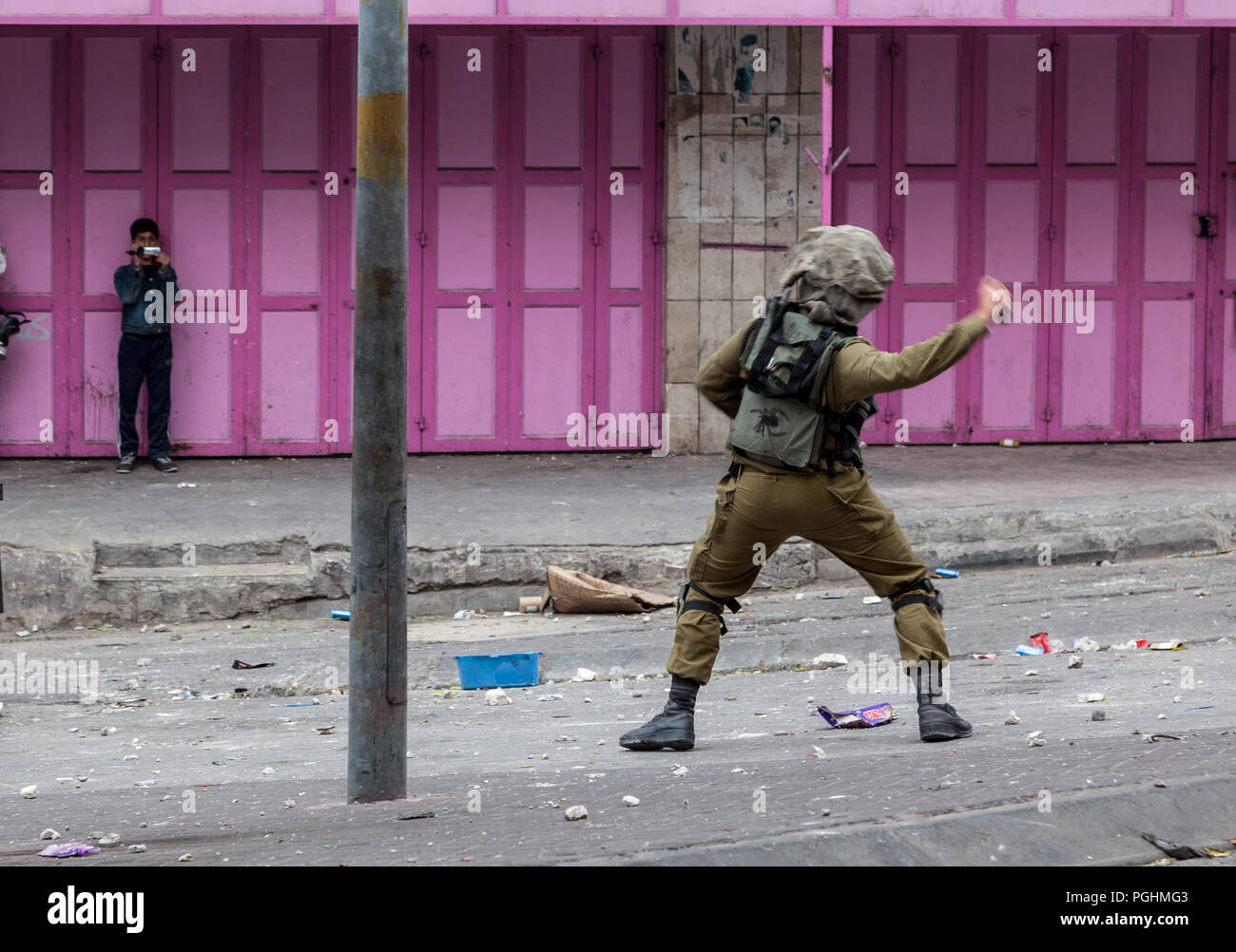 Hebron, Palestina, Novembre 29, 2013: Forze di Difesa Israeliane soldato è lanciare una granata a gas per disperdere i giovani palestinesi uomo durante disordini a Hebron Foto Stock