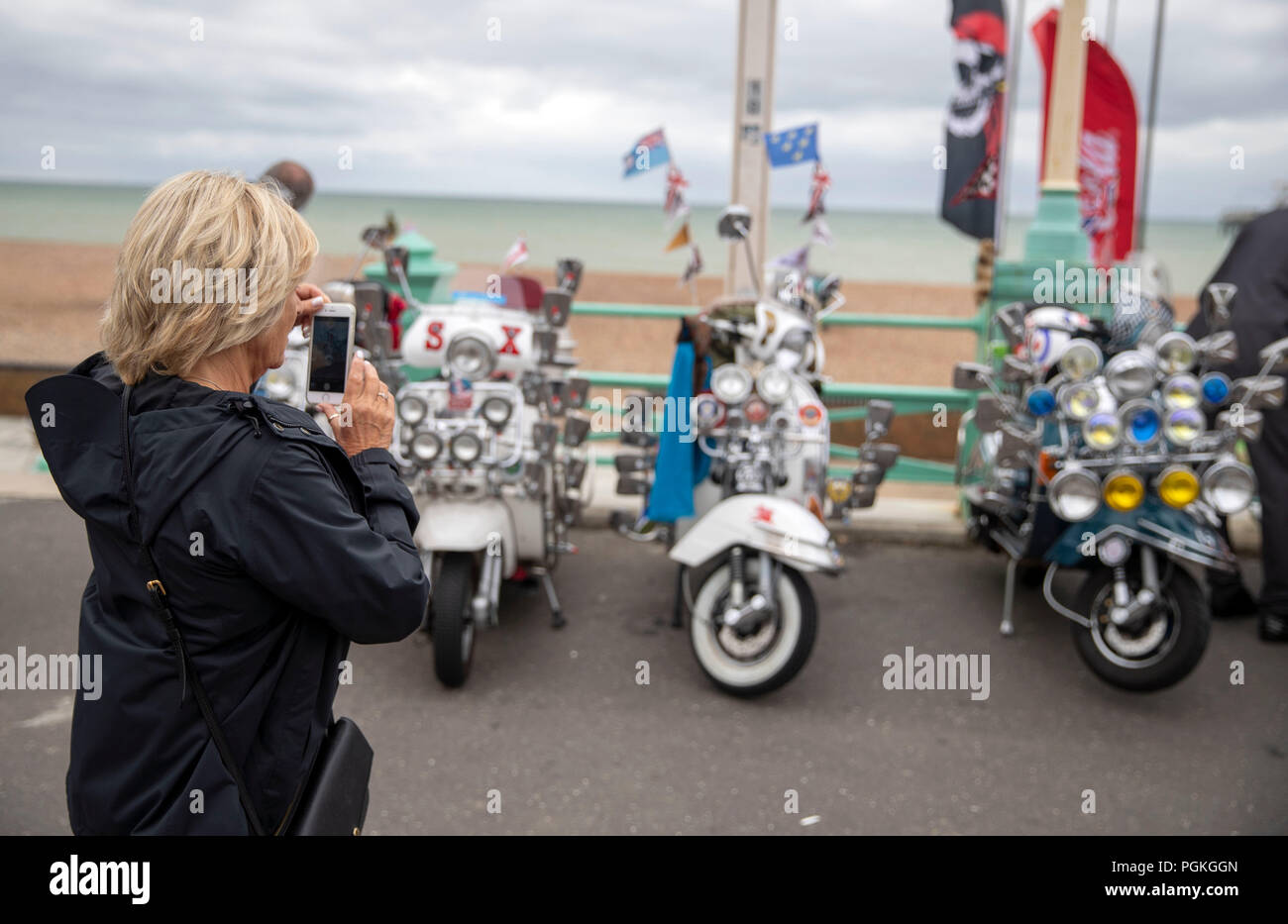 Una donna prende una foto di sessanta scooter parcheggiate accanto alla spiaggia di Brighton durante il Brighton Mod Weekender. Foto Stock