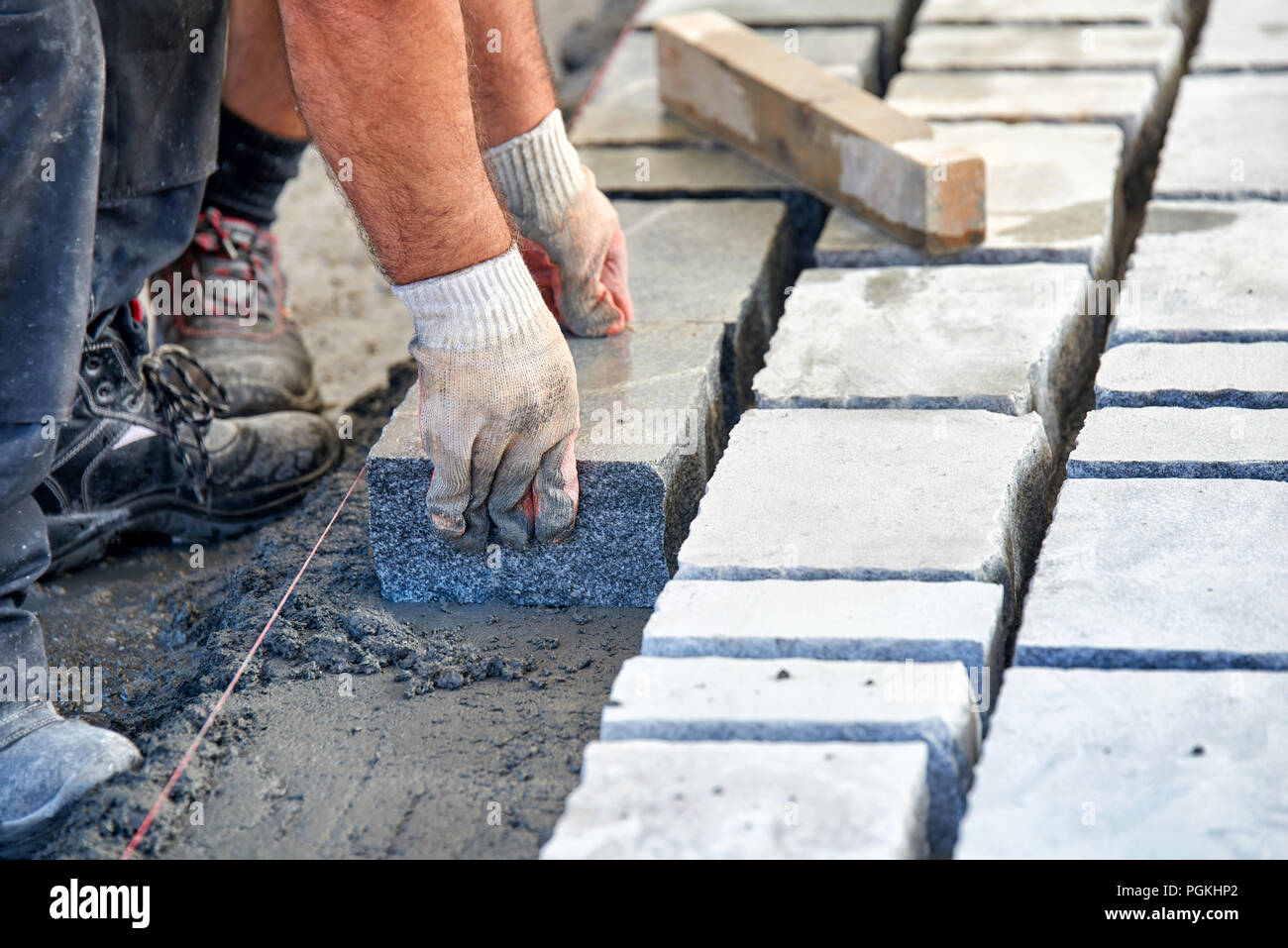 Un operaio di mani guantate utilizzare un martello per posizionare la pietra lastricatori. Lavoratore la creazione di pavimentazione utilizzando blocchi di ciottoli e massi di granito. Operaio industriale ho Foto Stock