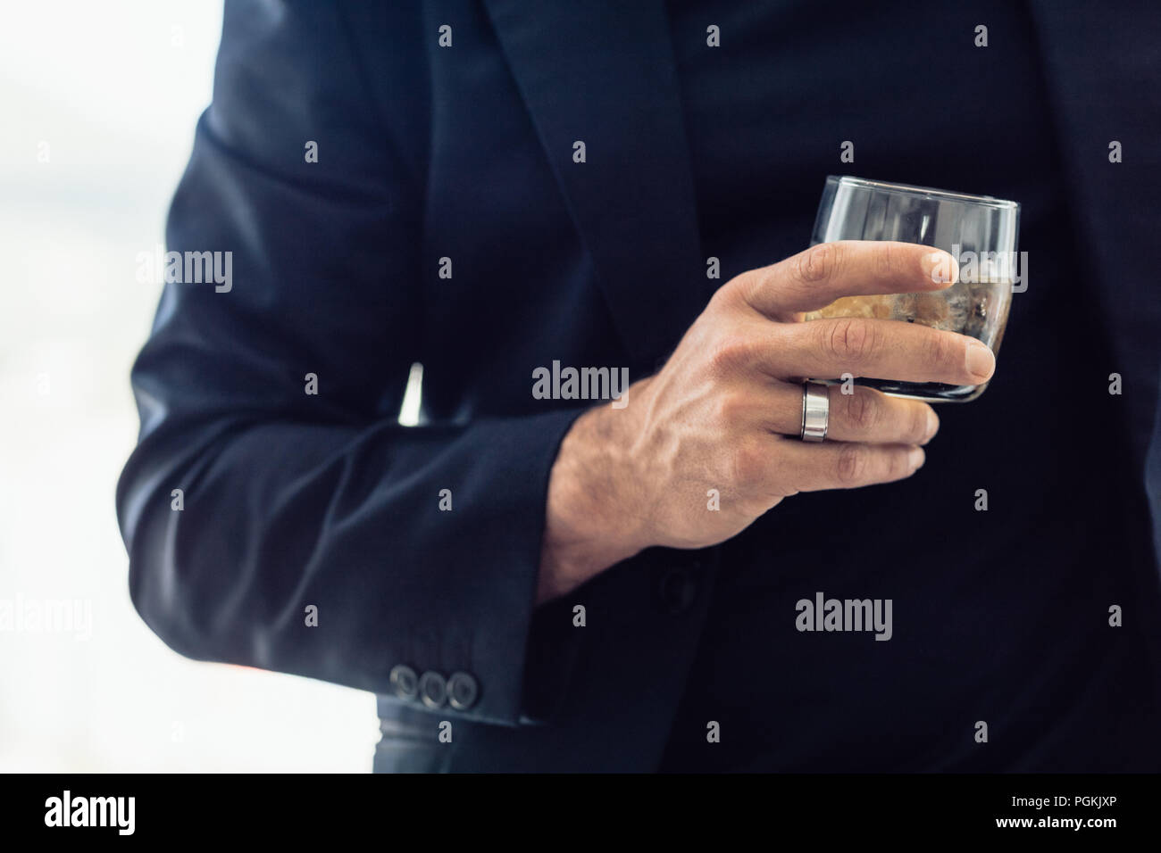 Stretta di mano imprenditore tenendo un bicchiere di whisky. Ritagliato shot dell uomo in abito nero con in mano un bicchiere di bibita in mano. Foto Stock
