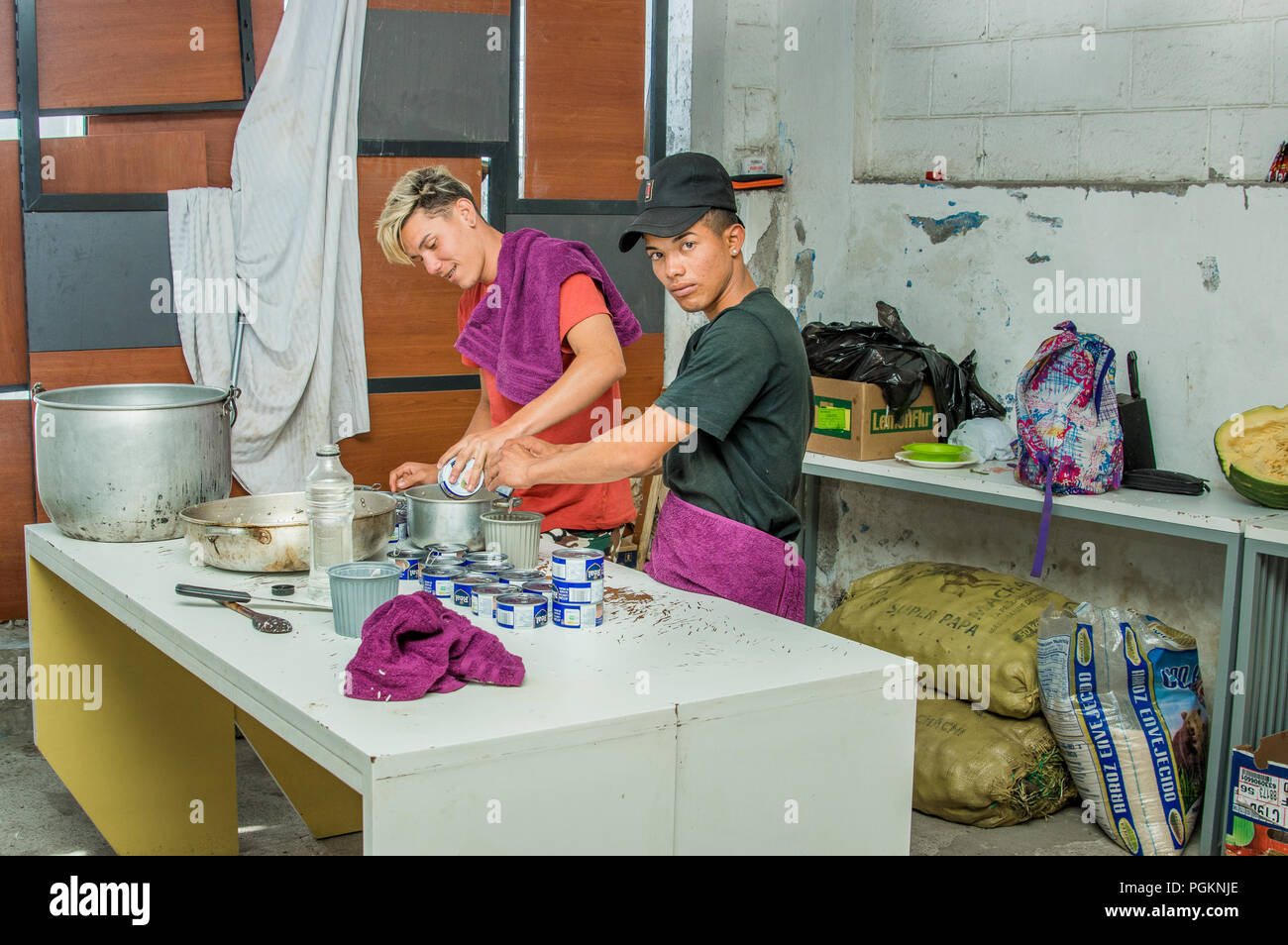 QUITO, ECUADOR, Agosto 21, 2018: Amici in cucina cucina la cena e aprire molte tonno può, all'interno di un rifugio per il popolo venezuelano che sfuggito f Foto Stock