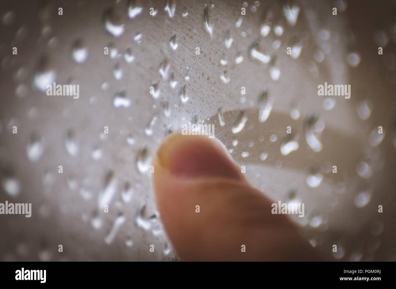 Moody sentimenti concetto: dito di un adolescente di disegno sulla finestra con le gocce di pioggia in un giorno di pioggia Foto Stock