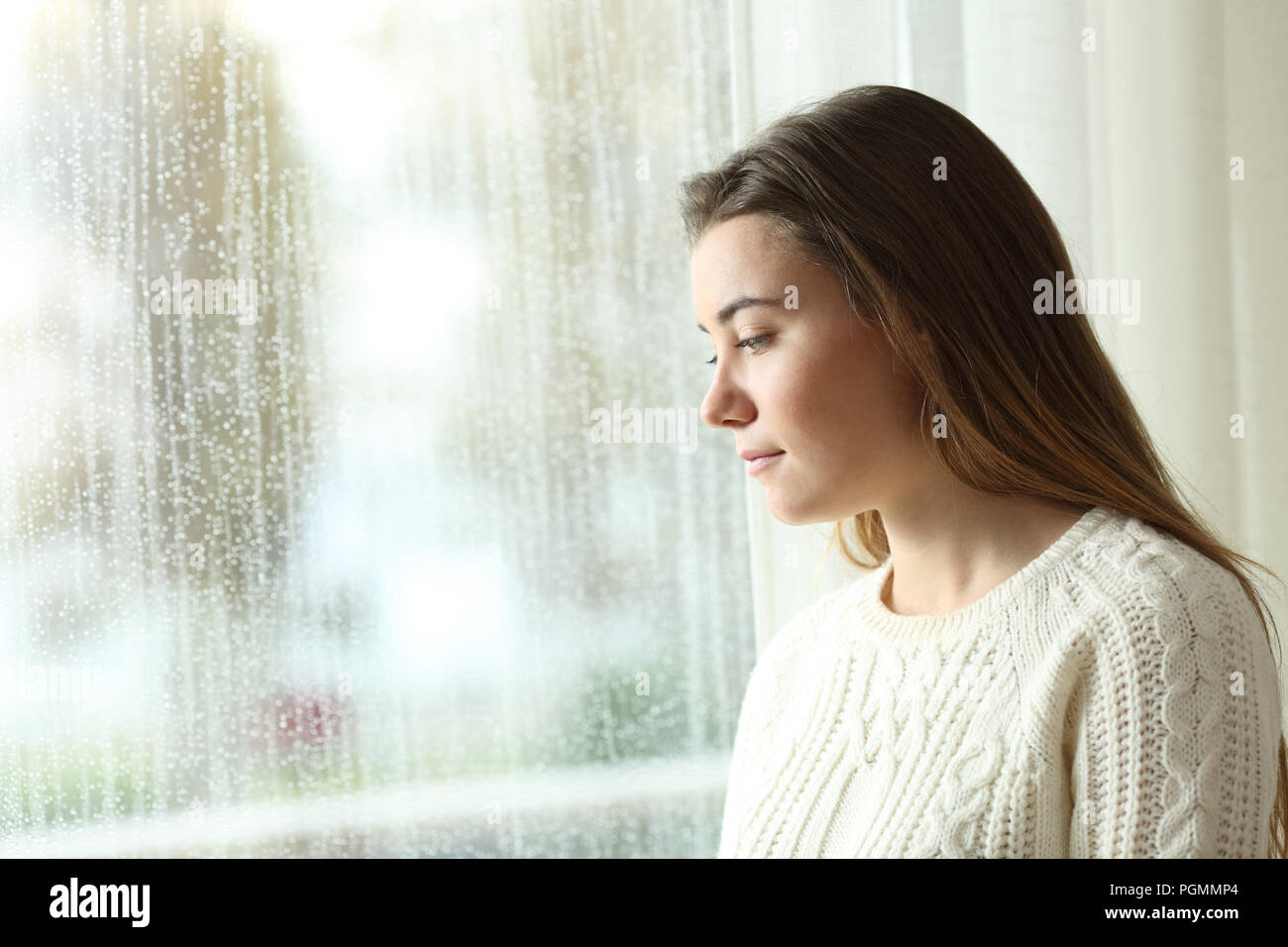 Triste donna che guarda all'esterno attraverso una finestra in un giorno di pioggia a casa Foto Stock