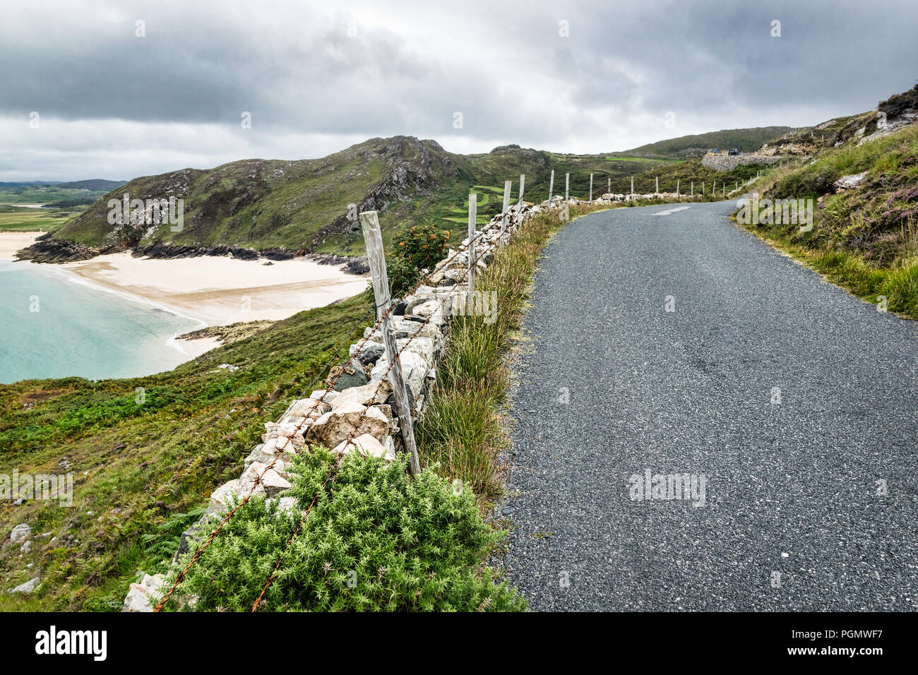 Questa è una strada a distanza la segue lungo la costa occidentale del Donegal Irlanda. Uno degli irlandesi spiagge può essere visto qui sotto le scogliere. Foto Stock