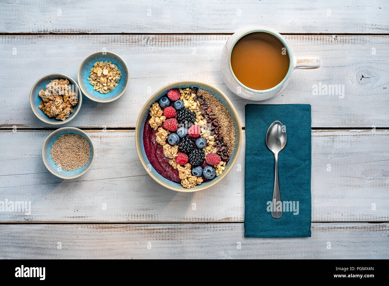 Una sana prima colazione. Ciotola frullato con frutti di bosco e noci, granola e una tazza di caffè sulla shabby white pannelli di legno. Appartamento laico, vista dall'alto. Foto Stock