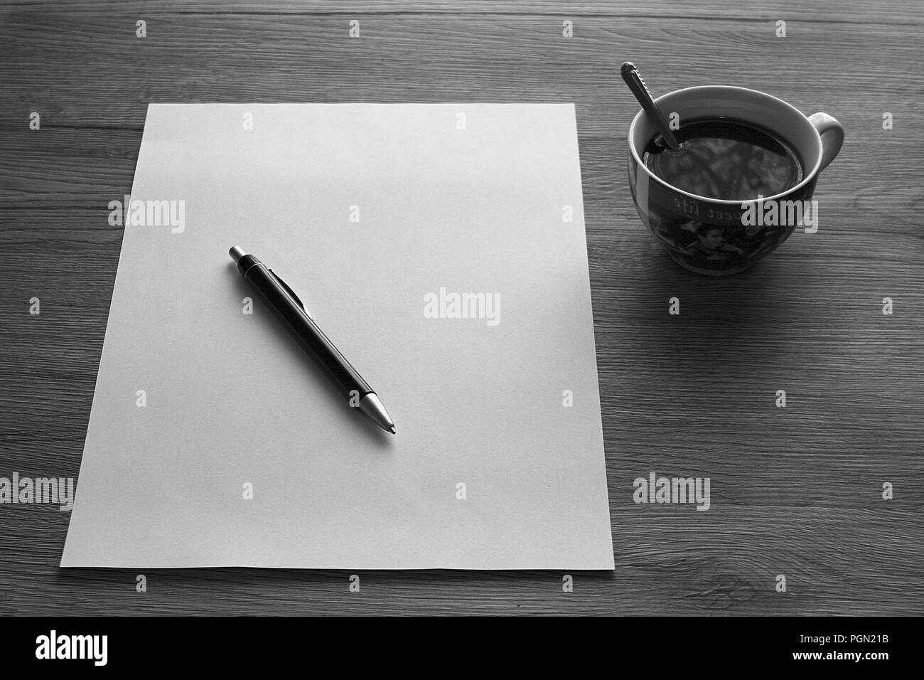 Ufficio in legno Scrivania con carta bianca, penna e una tazza di caffè a scala di grigi Foto Stock