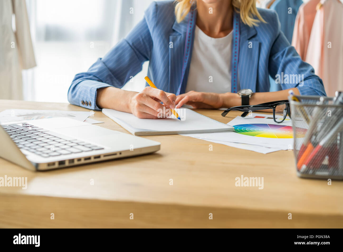 Trasformare le idee in capi di abbigliamento. Giovane e bella donna che lavorano su disegni nel suo studio vicino i vestiti appesi sulle cremagliere Foto Stock