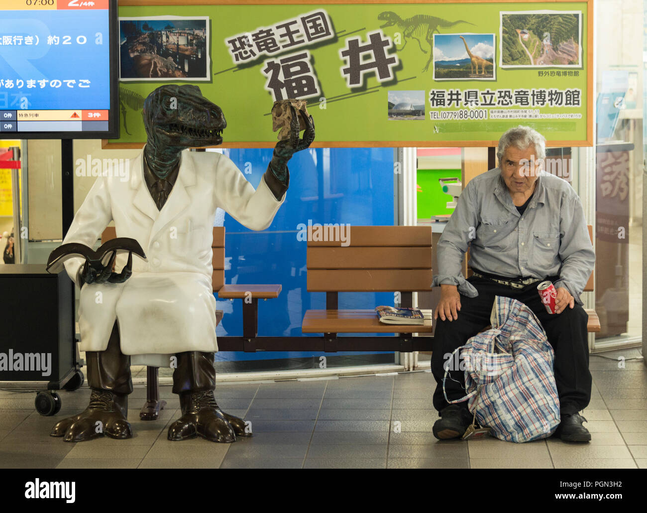 La foto mostra un uomo seduto accanto a una statua di dinosauro dentro la stazione ferroviaria in Katsuyama, Fukui Prefettura, in Giappone il 4 ottobre, 2016. Katsuyama è un Foto Stock