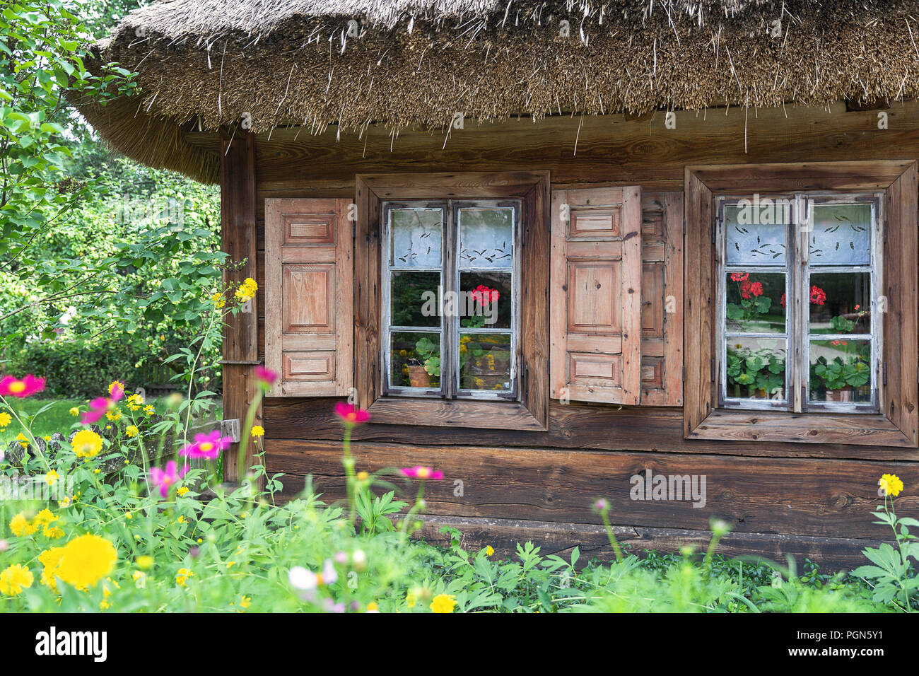Vecchia casa in legno con persiane widnow e circondato da fiori e alberi Foto Stock