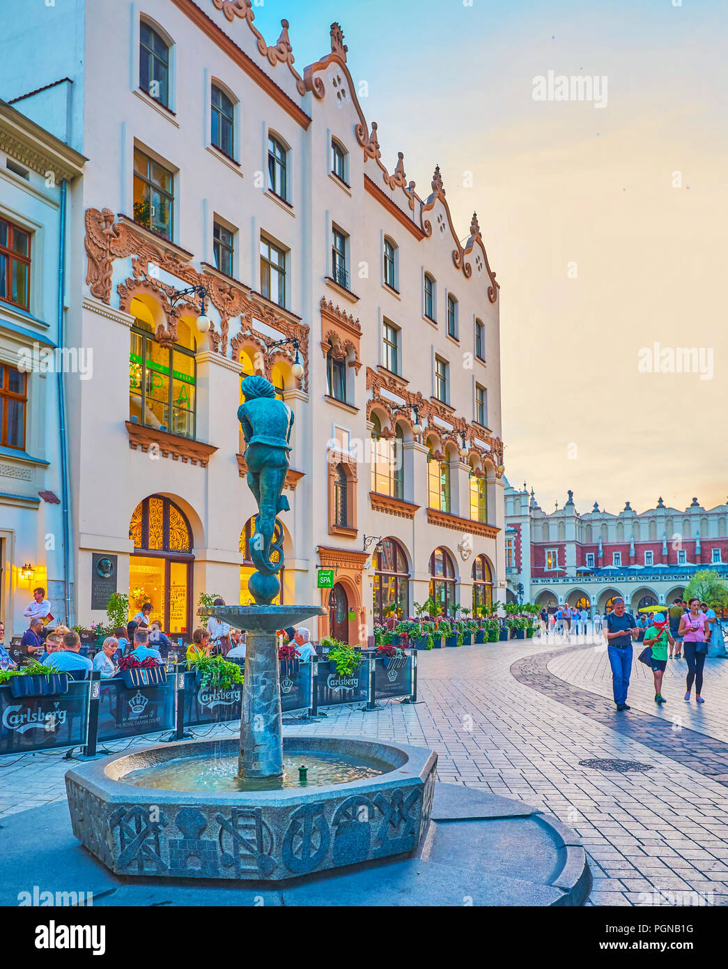 Cracovia in Polonia - Giugno 11, 2018: La scena urbana del centro storico di Cracovia con una piccola fontana con topper scultura di studente Zaka, e gli edifici del mercato principale S Foto Stock