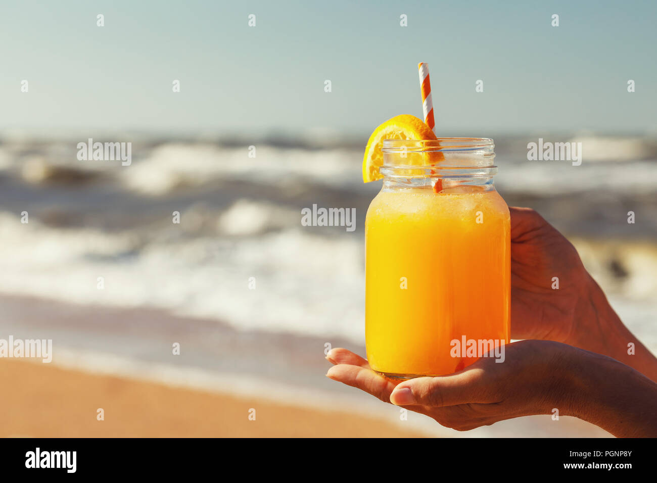 Succo di arancia con polpa in mani sulla spiaggia con spazio per il testo Foto Stock
