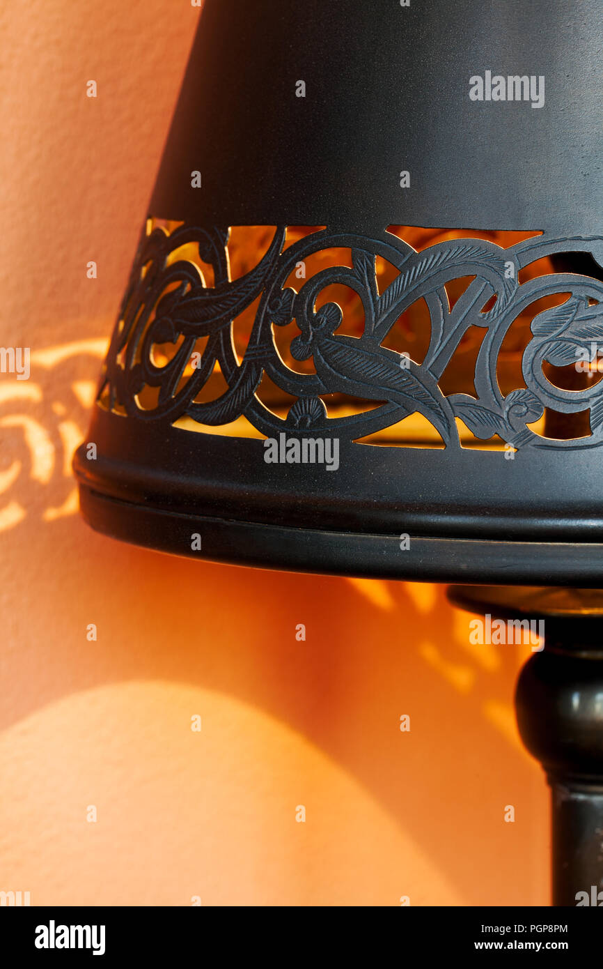 Decor marocchino. Trafitto di metallo nero lampada getta un ombra di pattern su una parete di colore arancione. Close up dettaglio. Posizione: Marrakech, Marocco Foto Stock
