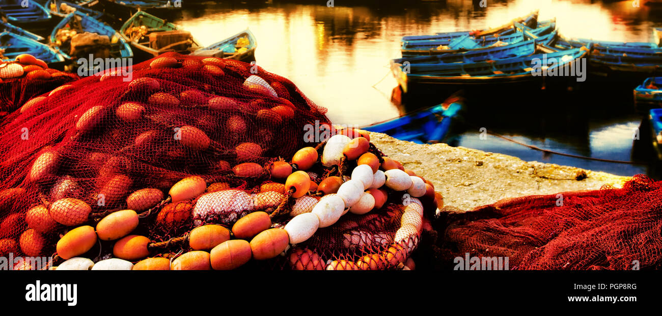 Il Marocco colorato lungomare vicino fino al tramonto di rosso le reti da pesca, arancio galleggianti, barche blu. Acqua oro colorate dal sole al tramonto. Posizione: Essaouira Foto Stock