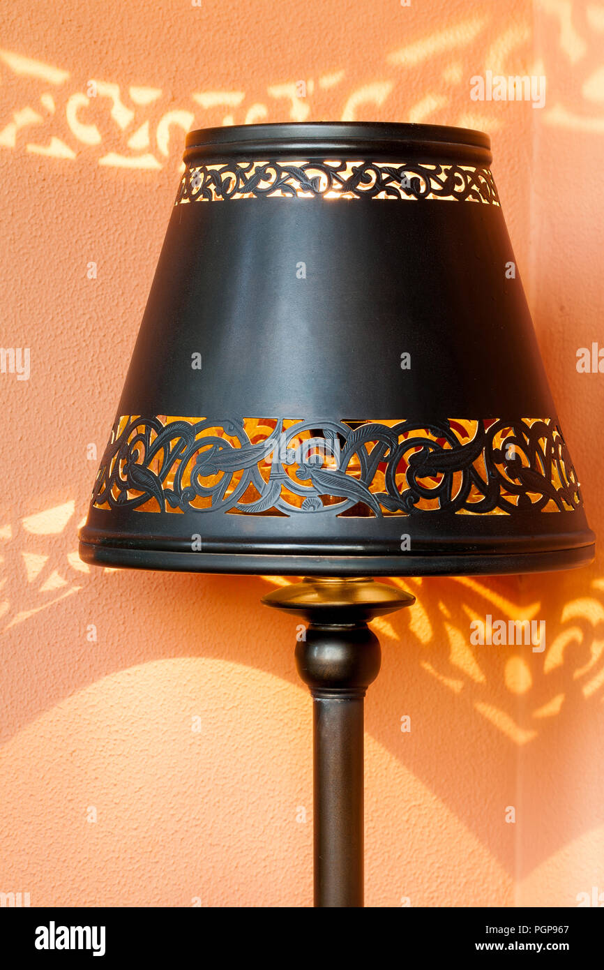 Il Marocco trafitto di metallo scuro lampada design ombra, gettando ombre sulla parete arancione. Esempio di marocchini stile decorativo. Posizione: Marrakech. Foto Stock