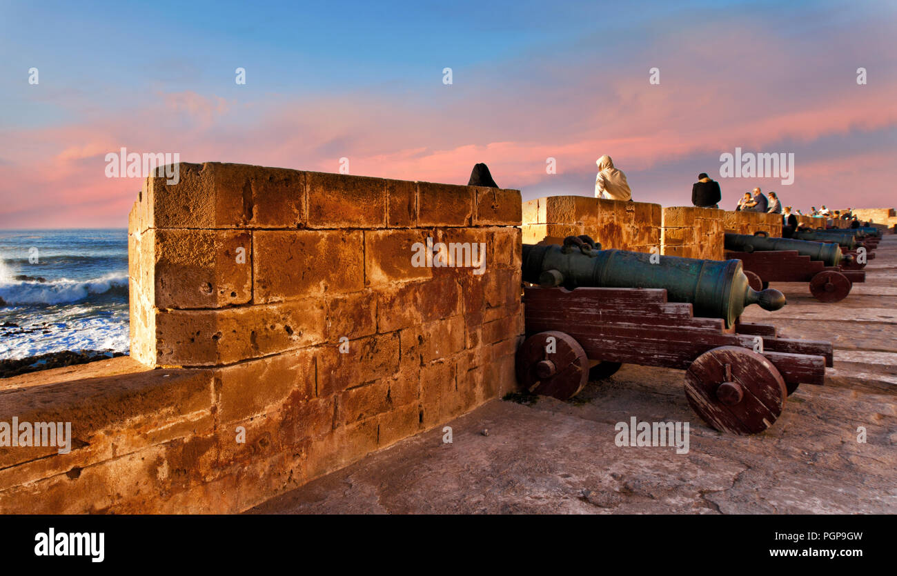 Marocco Essaouira le persone raccolgono e guardare il tramonto colorato dalle antiche mura fortificate in corrispondenza del bordo del villaggio sul mare. Consuetudini locali. Foto Stock