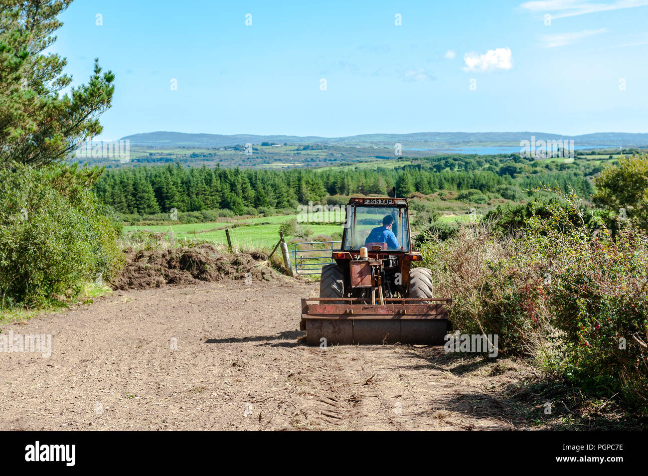 Agricoltore rotoli terreno dopo la semina di semi di erba in una giornata di sole in Ballydehob, West Cork, Irlanda con copia spazio. Foto Stock