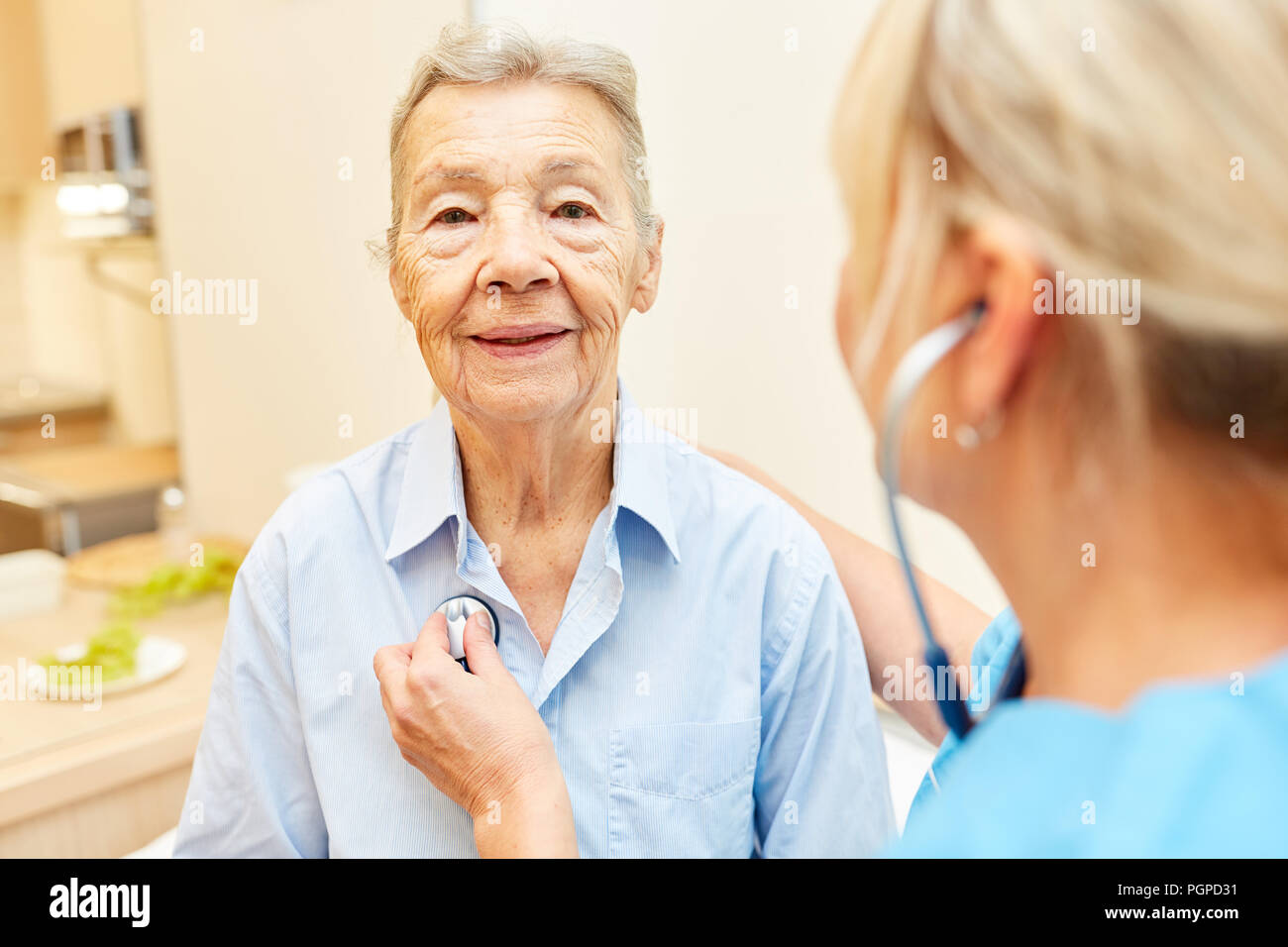 Medico o infermiere ascolta donna anziana con uno stetoscopio a casa Visita Foto Stock
