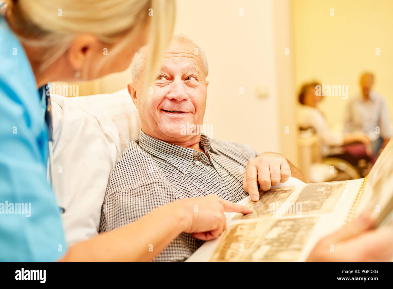 Uomo vecchio con il morbo di Alzheimer guarda foto album sotto la supervisione di un operatore sanitario Foto Stock