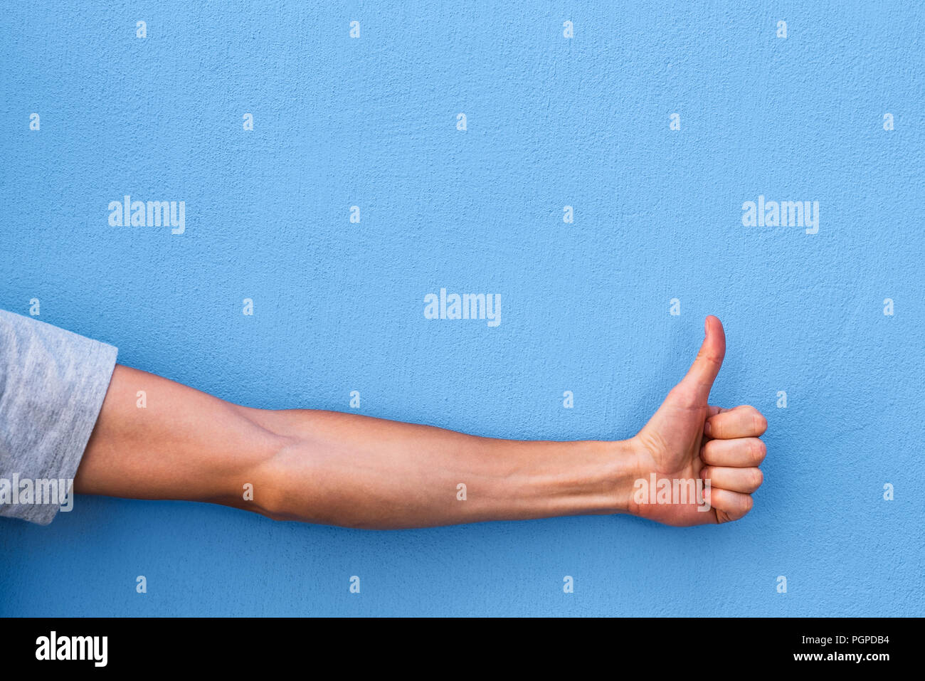 Gesto di approvazione e lode (Ok!). Pollice in su. Mano su uno sfondo blu con spazio di copia Foto Stock