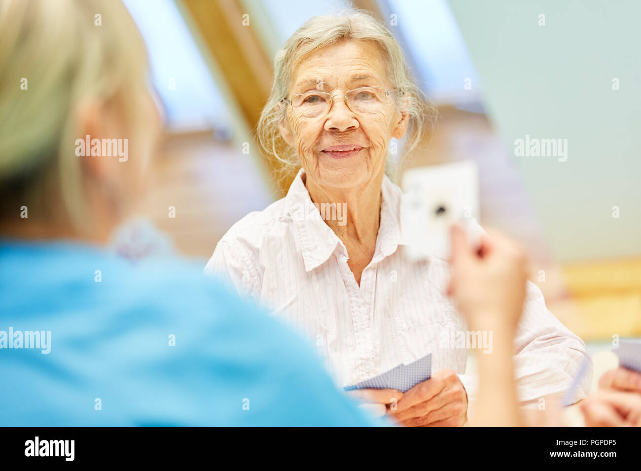 Donna anziana con demenza giocando a carte con la nutrice nella vita assistita Foto Stock