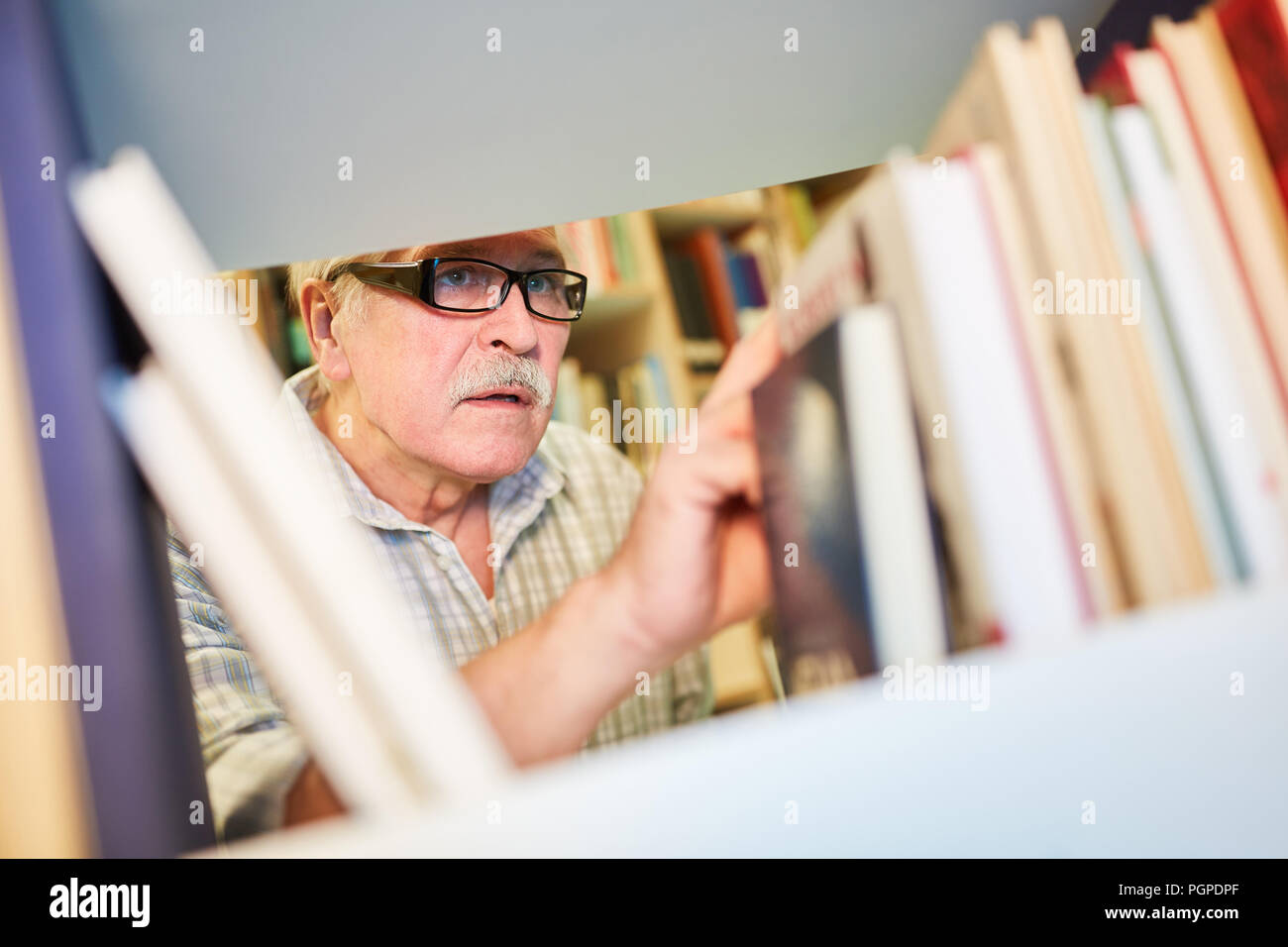 Senior uomo cerca libri mentre ricerca nella biblioteca presso la casa di riposo Foto Stock