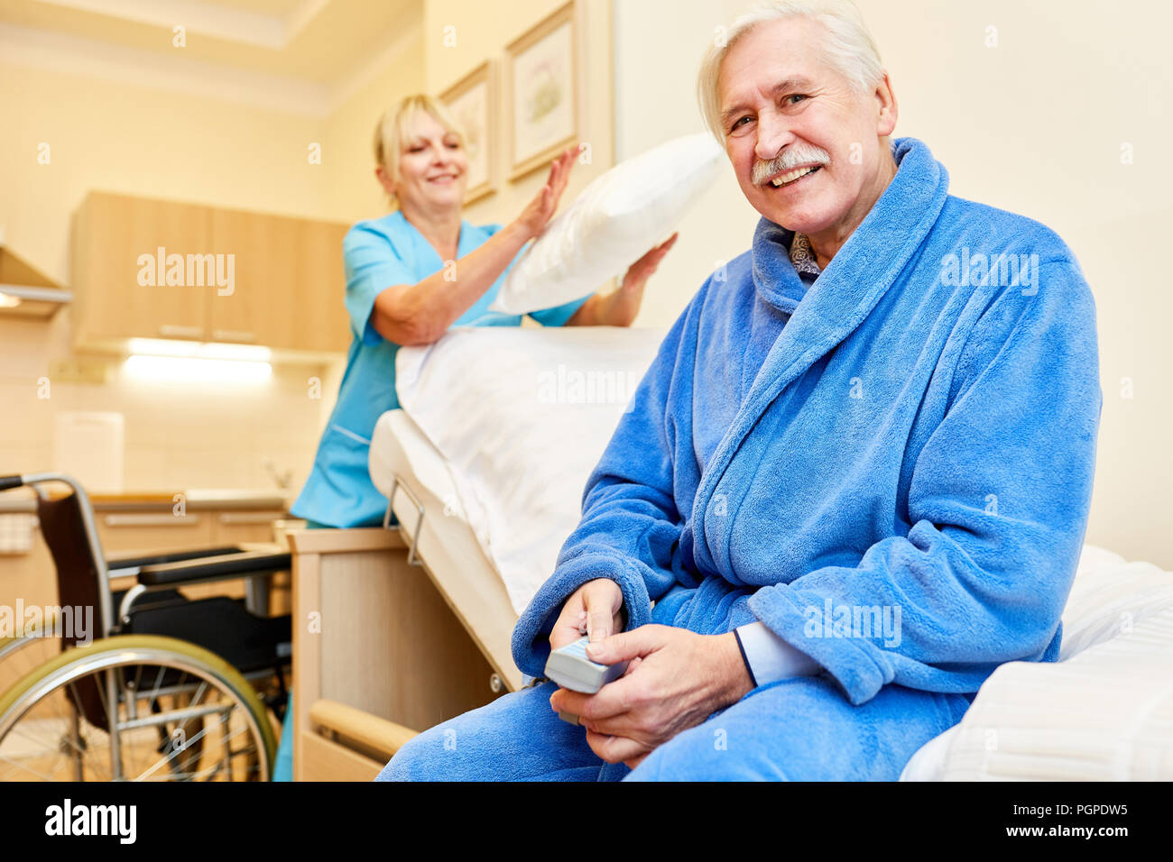 Senior uomo seduto sul letto di assistenza infermieristica in casa di cura con il caregiver Foto Stock