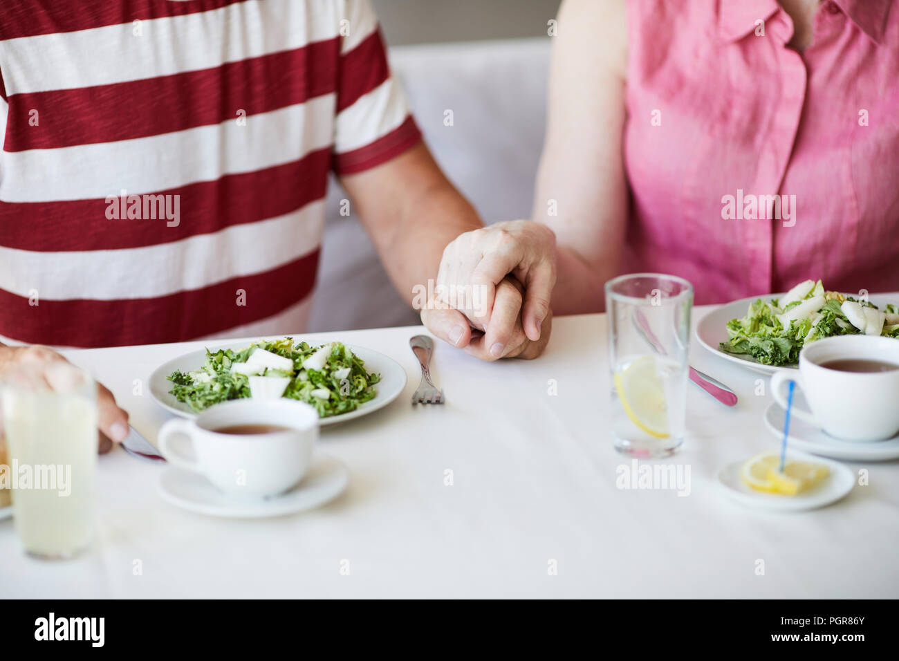 Donna matura tenendo il marito a mano mentre entrambi seduti a tavola durante il pranzo o la colazione Foto Stock