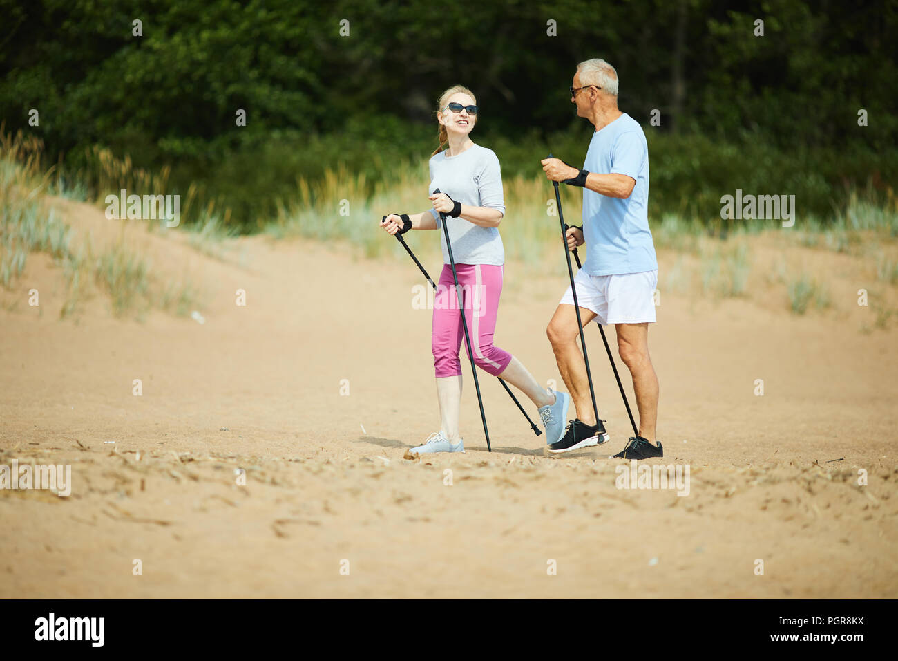 Uomo maturo e la donna in activewear parlando mentre passeggiate sulla spiaggia di sabbia Foto Stock