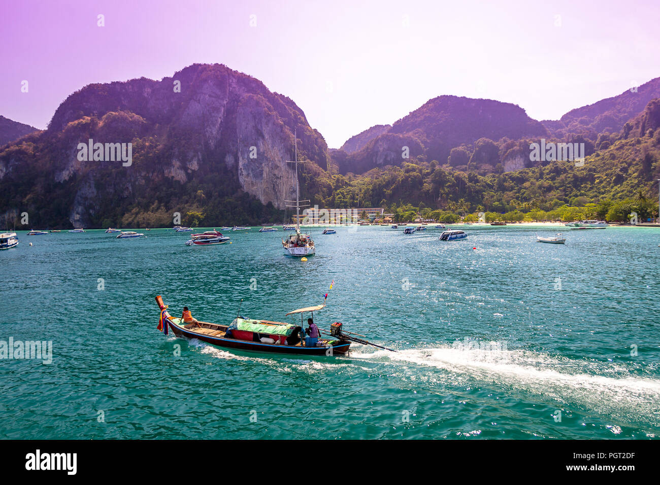 Un gruppo di barche in distanza con un piccolo uno andando con la sua scia seguenti. La Thailandia è occupato con barche e scogli di roccia in una giornata di sole. Foto Stock