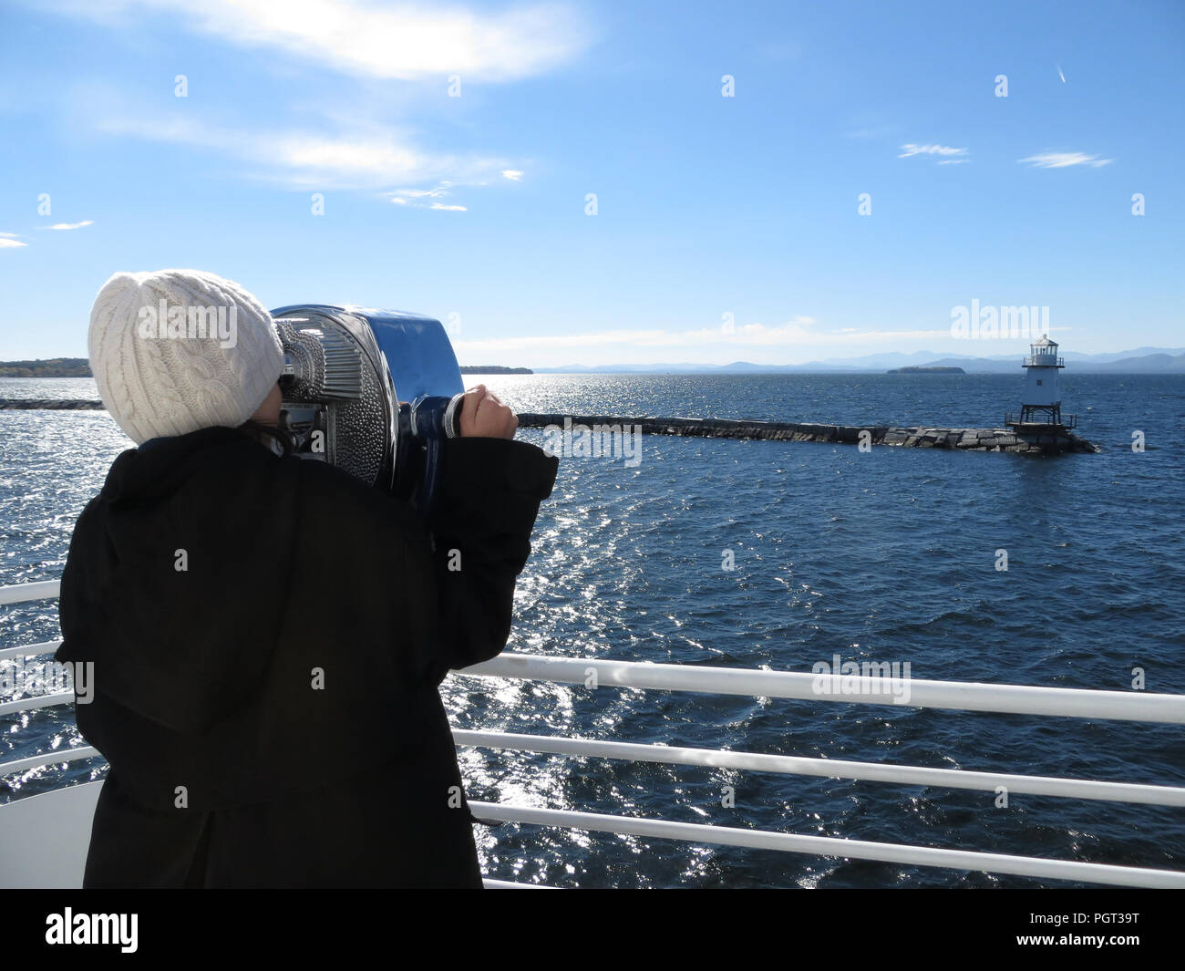 Giovane ragazza vestita per l'inverno, guardando attraverso il binocolo dal ponte di una barca al piccolo faro sul molo . Foto Stock