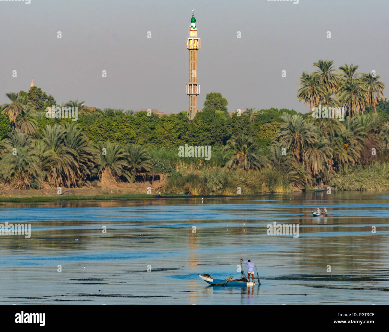 Egiziano uomo locale nella vecchia barca a remi la pesca con rete di mattina presto la luce del sole, con alto minareto della moschea, Fiume Nilo, Egitto, Africa Foto Stock