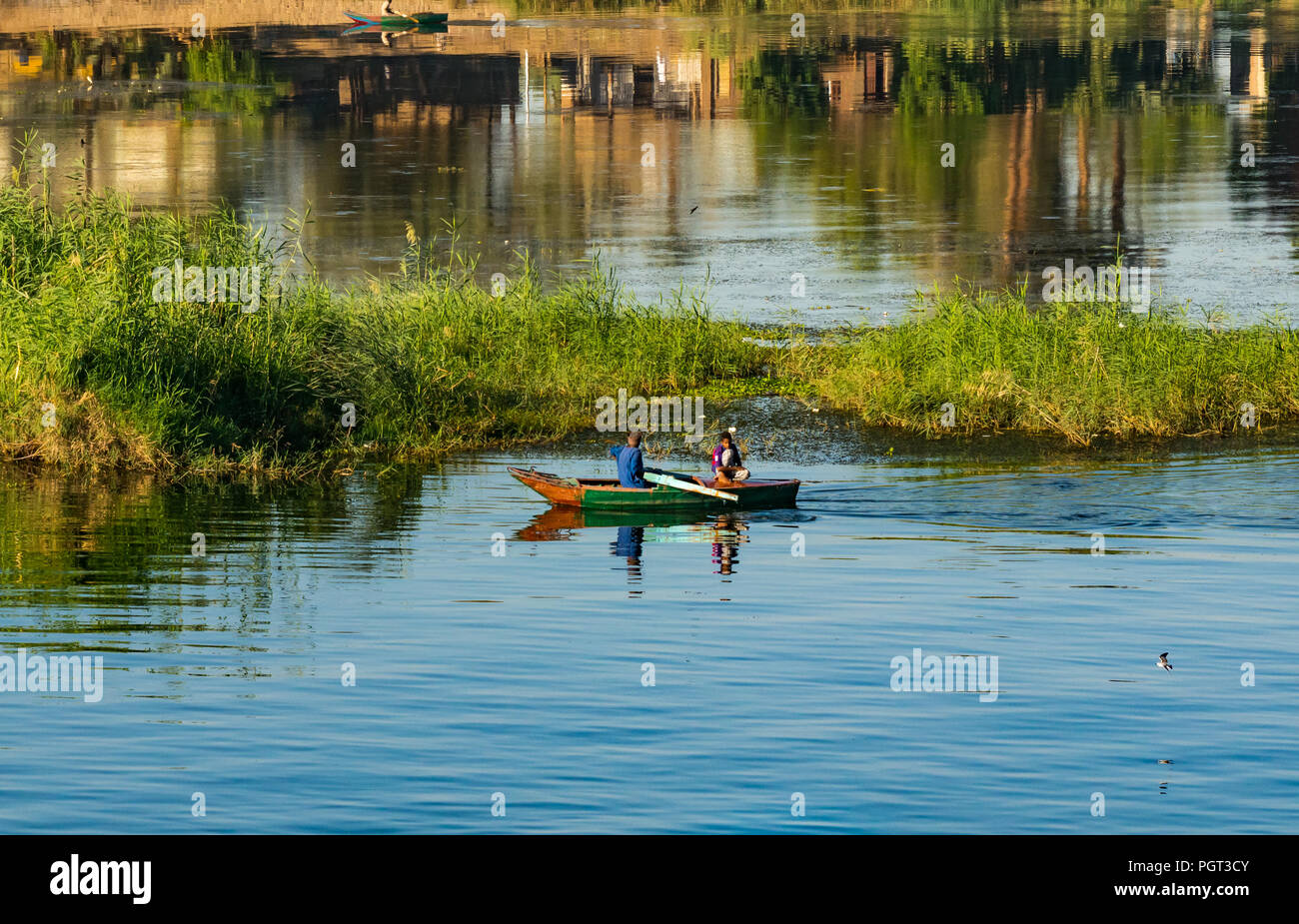 Locale egiziano uomo canottaggio vecchia barca con ragazzo di prima mattina la luce del sole, con riflessioni di acqua, Fiume Nilo, Egitto, Africa Foto Stock